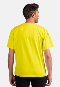 Žluté bavlněné tričko s uvolněným střihem a krátkými rukávy, s kulatým výstřihem a hladkým povrchem. Bez viditelných log nebo vzorů.