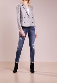 Šedý kostkovaný dvouřadý blazer s černými knoflíky, spárovaný s odrbanými džíny a černými lodičkami na kotníky.