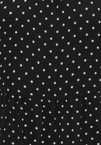 Fekete szövet egyenletesen elhelyezett kis fehér pöttyökkel és egy vízszintes varrással, amely fodros részletet hoz létre.