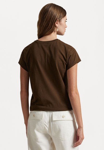 Brązowa bawełniana koszulka z krótkimi, podwiniętymi rękawami, okrągłym dekoltem i luźnym krojem, w zestawie z białymi spodniami z tylnymi kieszeniami.