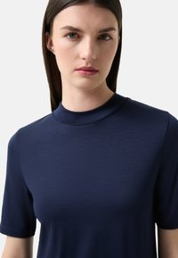 Námořnická modrá košile s krátkým rukávem a vysokým límcem, vyrobená z hladké tkaniny, s jednoduchým a čistým designem s minimálním zdobením.