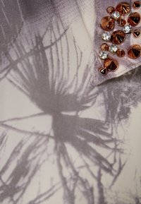 Strickstoff mit abstraktem grauem Blumenmuster, ausgestattet mit einem Kragen, der mit rosegoldenen und klaren Strasssteinen verziert ist.