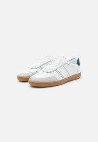 Sneaker bianche con tomaia in pelle liscia, dettagli in suede grigio, suola in gomma e un tab sul tallone verde. Lacci con sette occhielli.