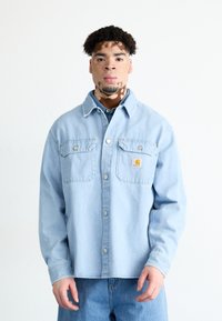 Gaiši zils džinsa krekls ar divām krūšu kabatām, snap pogām un Carhartt loga uzšuvi. Iespējas ir brīvs piegriezums un izturīgs materiāls.