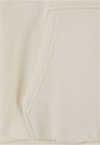 Crewneck sweatshirt i lys beige, med en frontlomme, teksturert stoff og ribbet kant. Sømmen er synlig langs sømmene.