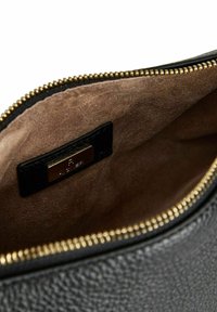 Interno di una borsa in pelle nera con una fodera marrone liscia, dotata di una cerniera dorata e di un piccolo etichetta nera con testo in rilievo.