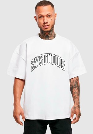Hvid oversized t-shirt lavet af bomuld, med fed sort tekst "ZY STUDIOS" i en buet design. Korte ærmer og afslappet pasform.