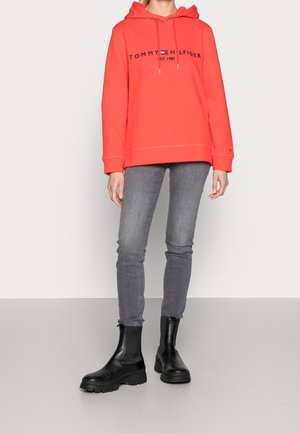 Koralowa bluza z kapturem z logo „Tommy Hilfiger” w granacie, zestawiona z szarymi, obcisłymi dżinsami i czarnymi botkami za kostkę.