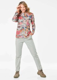 Langärmliges, mehrfarbiges Oberteil mit einem Blumenmuster, kombiniert mit hellgrauen Hosen und hellbraunen Wanderschuhen. Das Oberteil besitzt einen Rundhalsausschnitt und Taschen.