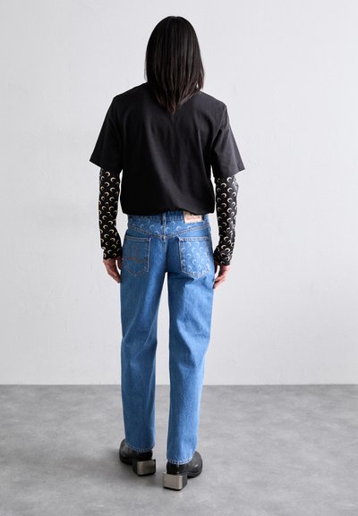 Svart t-shirt, långärmad mönstrad baslager, blå denimjeans och kraftigt sålda svarta skor. Anmärkningsvärd sömnad på jeansen.