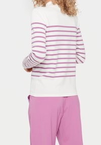 Camiseta de manga larga con una base blanca y rayas moradas horizontales, cuello redondo y un corte relajado, combinada con pantalones rosas.