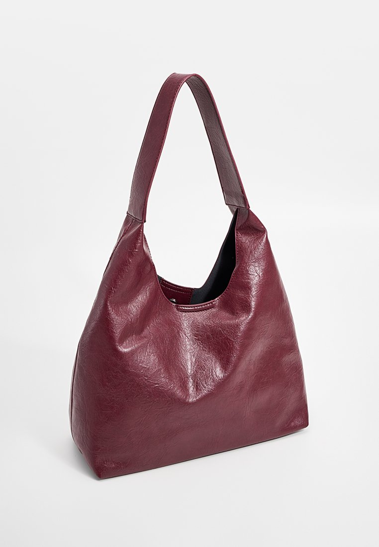Bolso hobo de cuero burdeos con un acabado suave y texturizado, asa única y diseño de abertura en la parte superior. Presenta un interior espacioso.