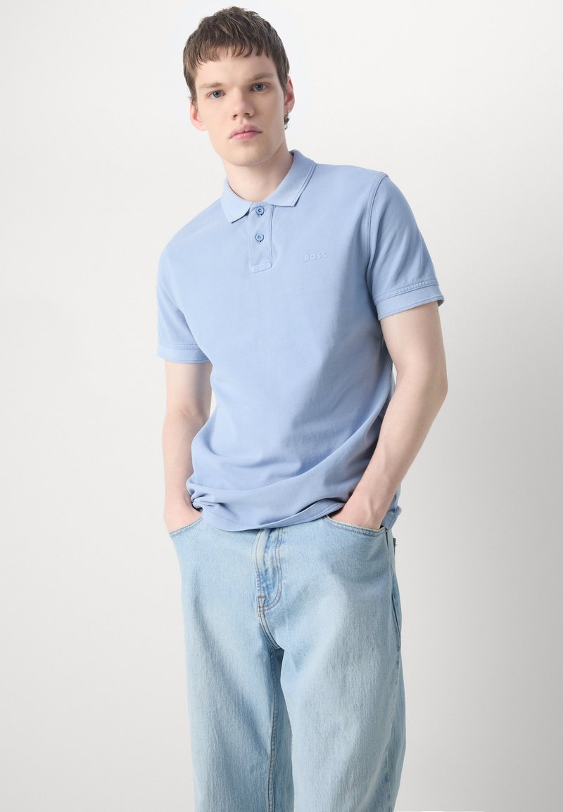 Polo shirt bleu clair avec un col pointu et une patte de boutonnage à deux boutons, associé à un jean en denim clair. Marquage subtil près de la poitrine.