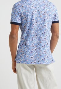 Kortärmad skjorta i ljusblått med blommönster, marinblå krage och en avslappnad passform. Tillverkad av bomull, med lätt rundad fåll.