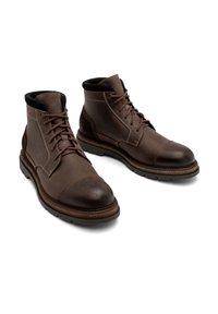 Brązowe skórzane botki za kostkę z okrągłym noskiem, sznurowane, z kontrastowymi ciemnymi akcentami. Solidna gumowa podeszwa z teksturowanym bieżnikiem.