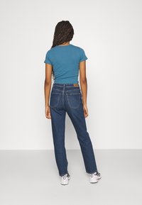 Camiseta de algodón azul y jeans de mezclilla azul oscuro, con un corte clásico, detalle en el bolsillo trasero y una cinturilla con una etiqueta de cuero.