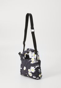 Geantă neagră matlasată cu margarete albe și accente galbene. Curea ajustabilă neagră, două mânere și închidere cu fermoar. Design compact, rectangular.