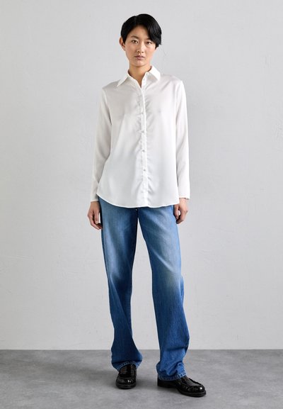 Blusa bianca a maniche lunghe realizzata in tessuto seta con abbottonatura frontale. Abbinata a jeans a gamba larga azzurri e scarpe eleganti nere.