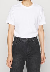 Witte crewneck t-shirt van katoen, met korte mouwen en een ontspannen pasvorm, gecombineerd met hoge zwarte denim jeans met knoopsluiting.