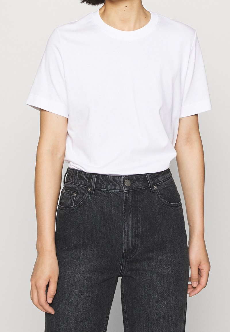 Witte crewneck t-shirt van katoen, met korte mouwen en een ontspannen pasvorm, gecombineerd met hoge zwarte denim jeans met knoopsluiting.