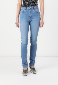 Jeans de tiro alto en azul claro con un corte ajustado, que cuentan con cinco bolsillos y un suave efecto de desgaste. Llevados con zapatos plateados de cordones.