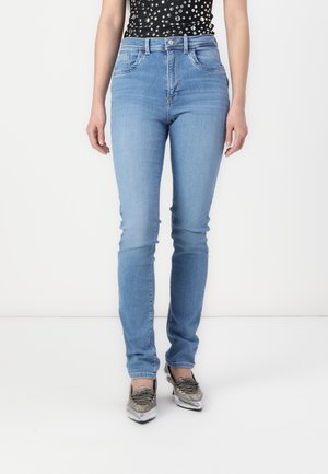 Jean taille haute bleu clair avec une coupe slim, comportant cinq poches et une légère décoloration. Portés avec des chaussures à lacets argentées.