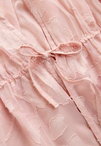Tissu rose clair avec un motif floral texturé et un cordon de serrage noué au niveau de la taille froncée.