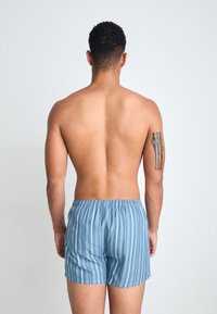 Bañador a rayas azul claro con una cinturilla elástica, visto desde atrás en una persona con un tatuaje en su brazo derecho.