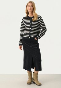 Striped cardigan in navy and cream, featuring a round neckline and button closure, paired with a black corduroy skirt with a front slit.