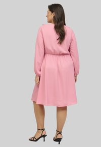 Rote Bluse mit langen, schmalen Ärmeln, elastischem Bund und fließendem Rock. Glattes Material und knielanges Design. Schwarze Riemchenabsätze.