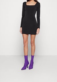 Svart långärmad mini-klänning med fyrkantig halsringning, matchad med lila spetsiga ankelstövlar med hög klack. Slät textur.