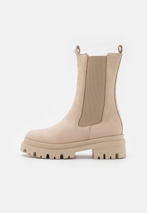 Beige ankelstøvler med en glat ruskindsfinish, elastiske sidepaneler og en chunky, tekstureret sål. Har løkkede træktab på bagsiden.