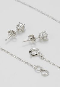 Pendientes de plata con respaldos decorativos, y una cadena delicada con un cierre de langosta y un colgante. Acabado suave y brillante con detalles intrincados.
