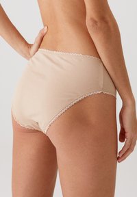 Beige katoenen slipjes met een gladde textuur, voorzien van delicate kantafwerking langs de tailleband en beenopeningen, zijaanzicht.