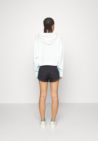 Vit kortad hoodie, svarta shorts med sidopaneler, och vita sneakers med turkosa detaljer. Slät textur, avslappnad passform.