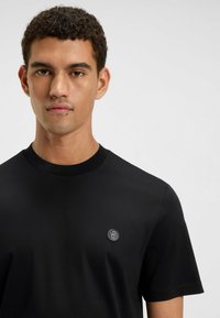 Czarna koszulka z bawełny z okrągłym dekoltem. Posiada małe, okrągłe logo na lewej piersi. Gładka tekstura, krótkie rękawy.