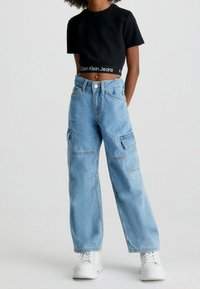 Černé zkrácené tričko s logem "Calvin Klein Jeans", kombinované se světle modrými oversized cargo džíny s bočními kapsami a volným střihem.