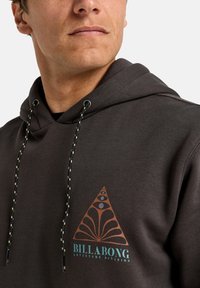 Dark gray hoodie with a triangular graphic design in brown and teal. Features drawstrings with a black and yellow pattern.