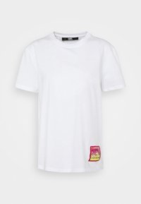 Camiseta de algodón blanca con cuello redondo y mangas cortas. Destacada con un parche rosa y amarillo en la parte inferior izquierda.