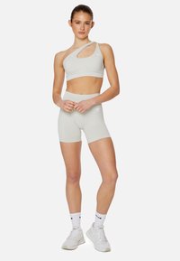 Lichtgrijze sportbeha met een asymmetrisch ontwerp en uitsnijding, gecombineerd met bijpassende hoge shorts. De stof lijkt glad en rekbaar.