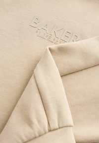 Beige mikina s textúrovanou tkaninou, s embosovaným logom "BAKER". Mäkké, priliehajúce manžety a nenápadný šikmý šev.