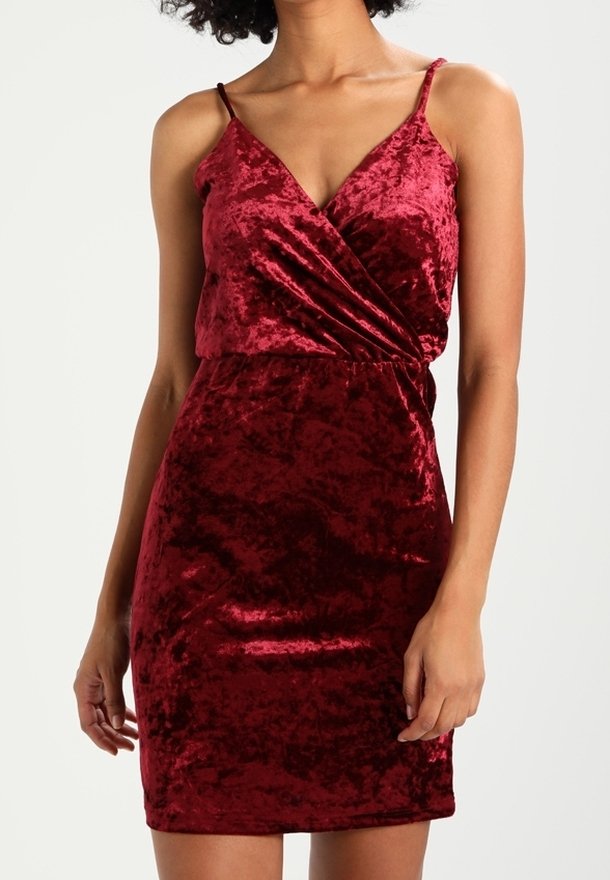 Robe mini en velours rouge avec de fines bretelles, design enveloppant et coupe moulante. Texture lisse, surface brillante et légère brillance tout au long.