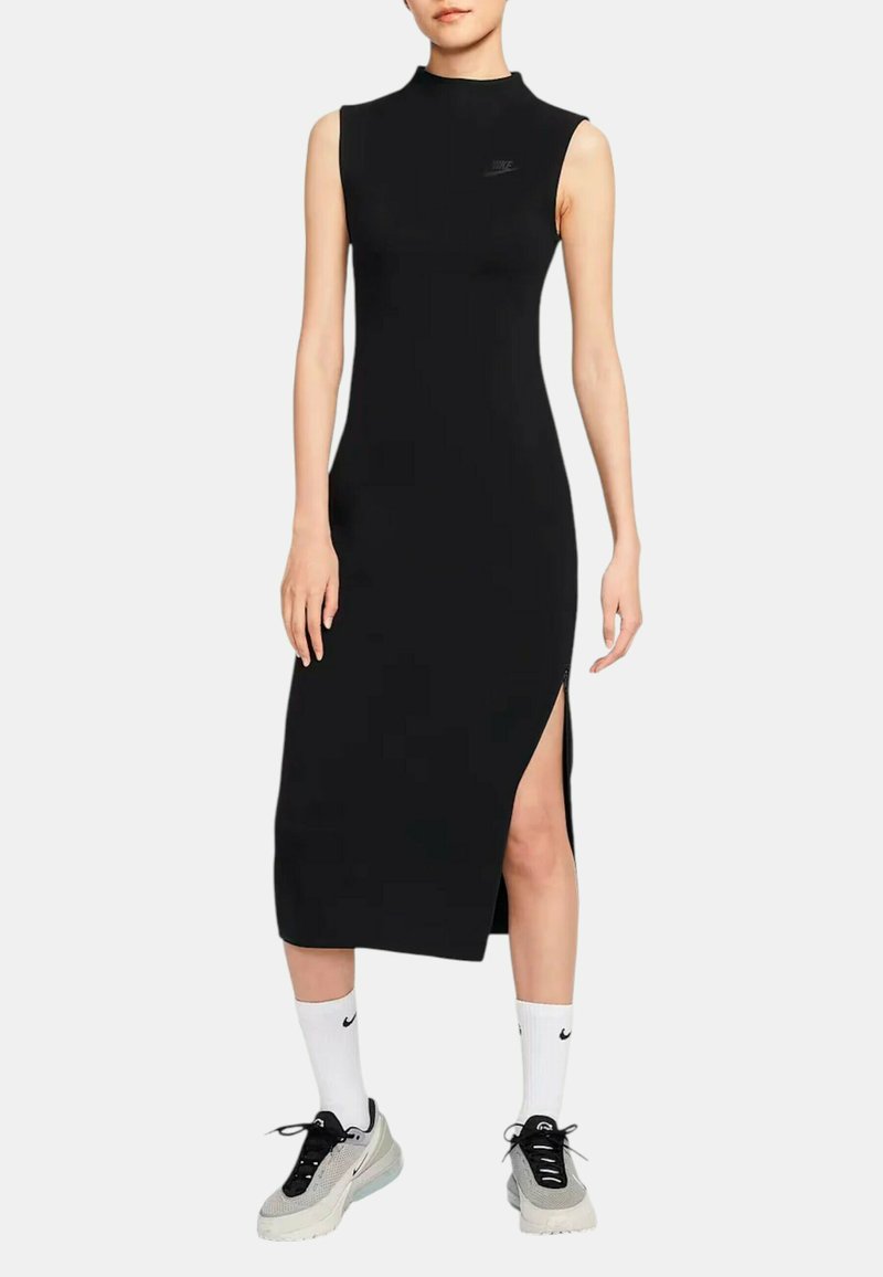 Vestito nero senza maniche con collo alto, spacchi laterali, realizzato in tessuto elasticizzato, con un piccolo logo sul petto. Indossato con sneakers sportive.