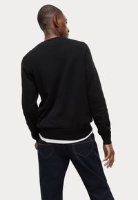 Czarna bluza z okrągłym dekoltem, ściągaczami przy rękawach i u dołu. Połączona z ciemnymi dżinsami. Gładka tekstura materiału, minimalistyczny design.