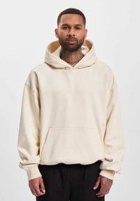 Crème-kleurige hoodie met een grote trekkoordkap, een voorzak en een relaxed fit. Zachte stof en ribbelboorden.