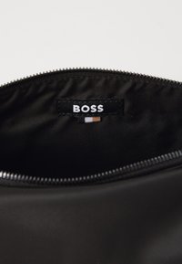 Crna najlon torbica sa zatvaračem na munju, unutra ima markirnu oznaku koja glasi "BOSS", a ukrašena je bijelim, smeškim i narandžastim prugama.