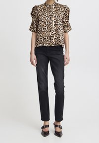 Blouse à imprimé léopard avec des manches courtes bouffantes, jean skinny noir, et chaussures à bout pointu de couleur sombre avec des brides de cheville.