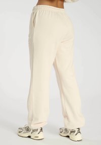 Light beige sweatpants with a drawstring waist, side pockets, and a loose fit. Material appears soft and textured with subtle branding detail.