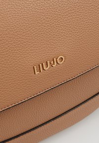 Tan gekruide leren tas met gouden LIU JO-logo en zwarte randdetail langs de randen.