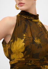 Abito halter marrone con motivo floreale, colletto plissettato in un tessuto leggero; presenta dettagli gialli e neri e spalline aperte.